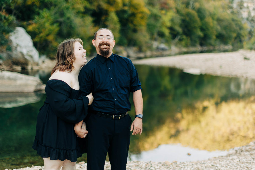 a couple hold each other and laugh with a mirror-like pool in the background