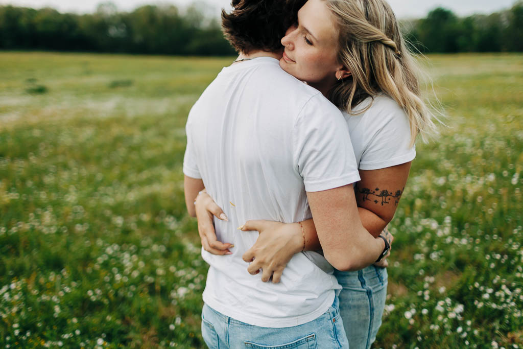 young couple embrace in a green field full of flowers
